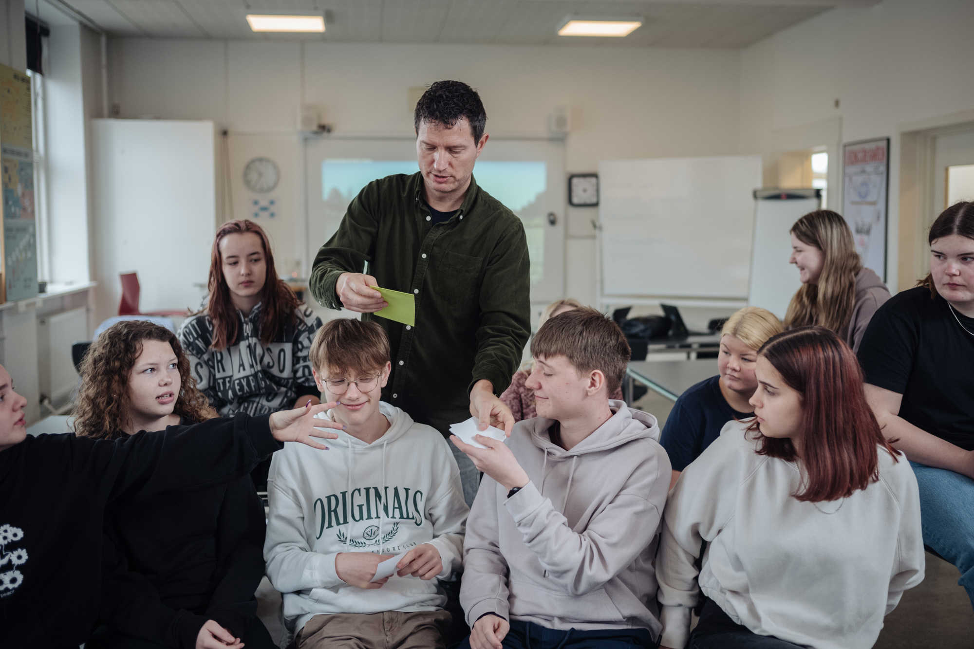 Billede af undervisningsituation med skolelederen og en gruppe elever, der modtager papirlapper.